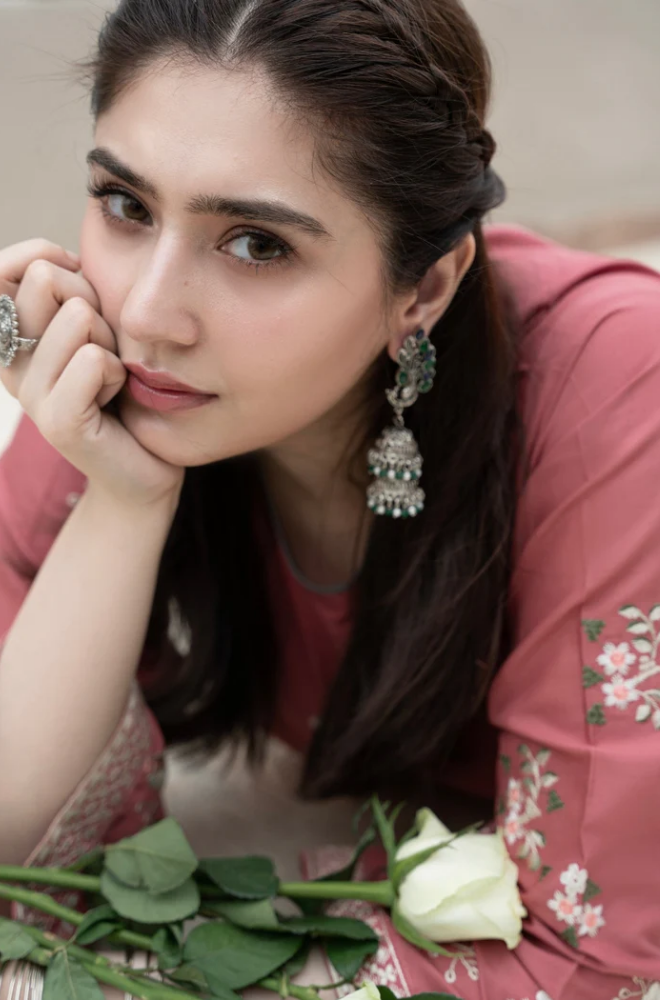 A woman in a pink dress sits on the ground surrounded by colorful flowers, enjoying a serene moment in nature.